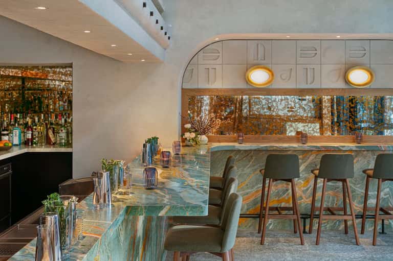Modern hotel bar with marble countertop, wooden accents, and gold pendant lighting fixtures