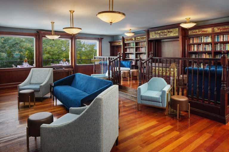 Elegant library lounge with dark wood shelving, fireplace, blue sofa, and large windows