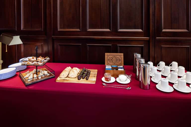 Elegant buffet spread with pastries, bread, olives, coffee cups on red tablecloth