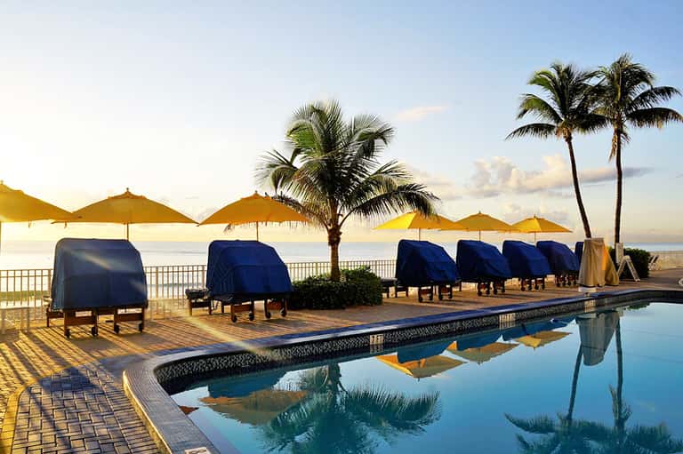 Oceanfront pool at sunset with yellow umbrellas, palm trees, and calm water reflections