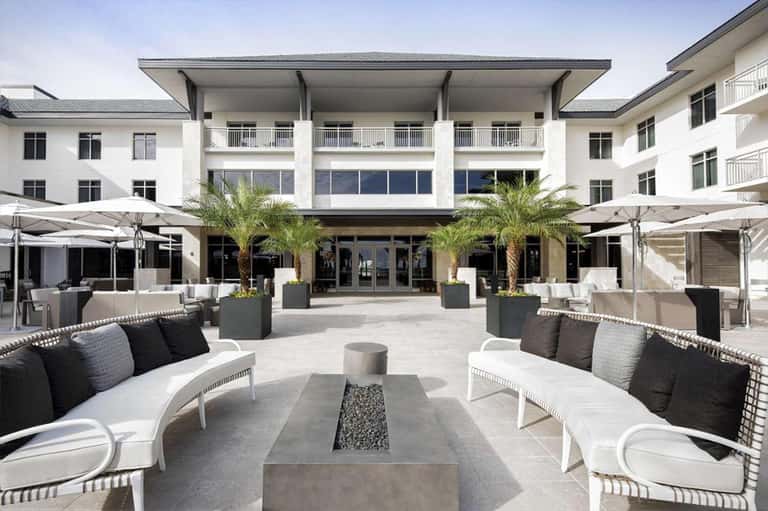 Modern hotel courtyard with fire pit seating, palm trees, and contemporary architecture