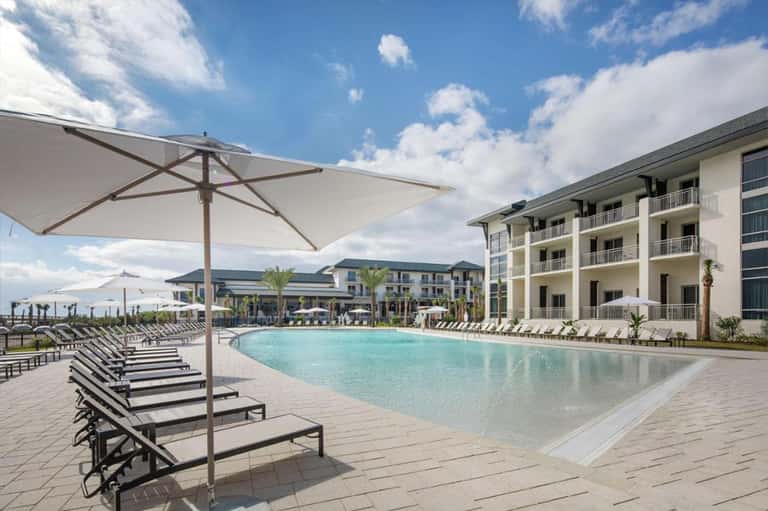 Resort pool area with striped loungers, umbrellas, and multi-story hotel building