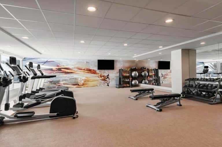 Fitness center with exercise equipment, treadmills, weights, and motivational wall graphics under ceiling lights