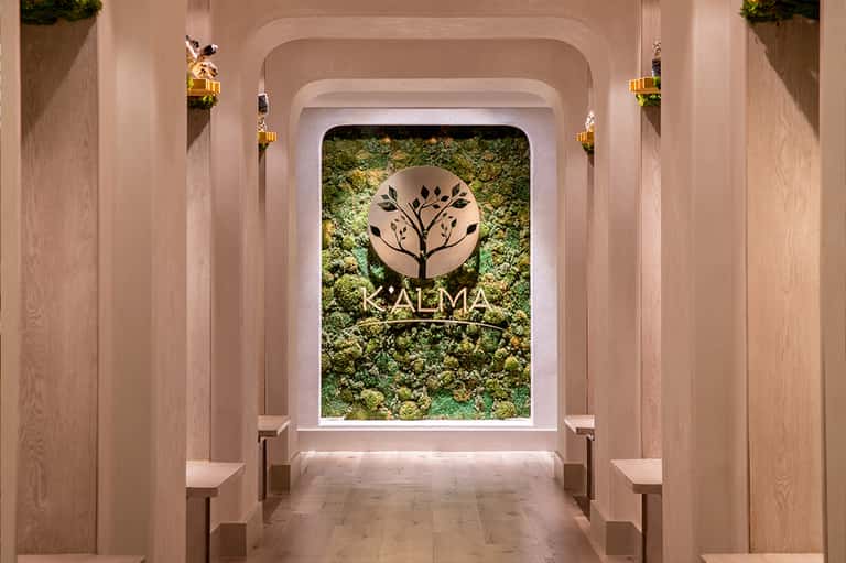 Modern spa entrance with moss wall and KALMA logo under rounded archway with wooden paneling
