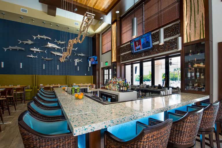 Upscale bar interior with blue accent wall, decorative fish mobile, terrazzo countertop, and coastal décor
