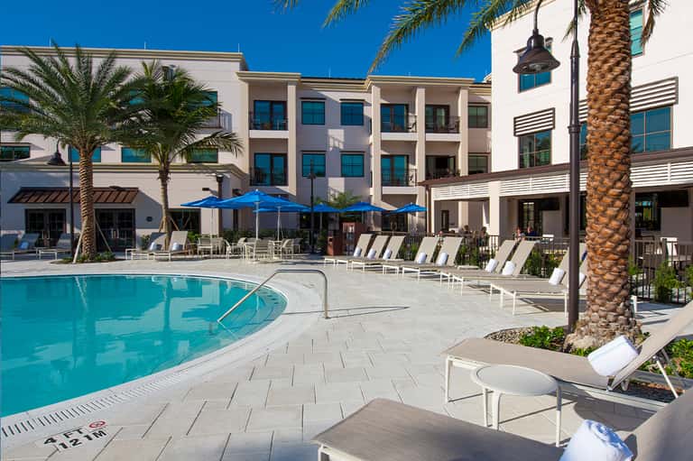 Resort pool courtyard with blue umbrellas, palm trees, white lounge chairs, modern architecture