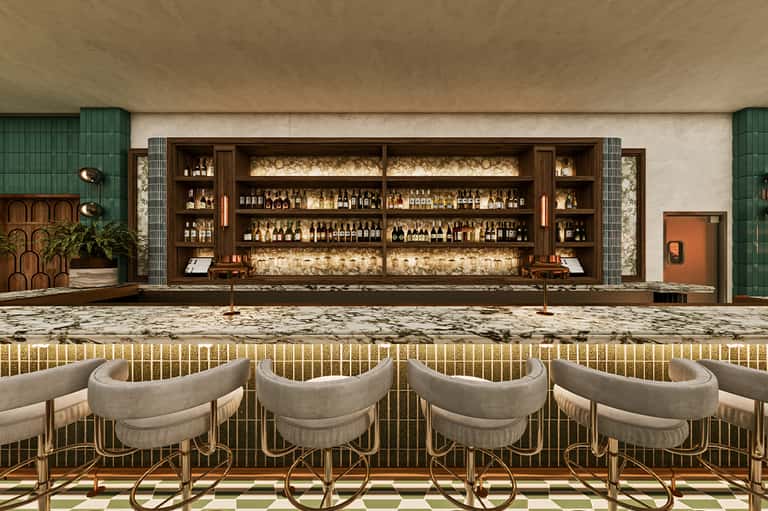 Upscale bar interior with wood-backed shelving displaying bottles, cream curved bar stools, and green accent wall