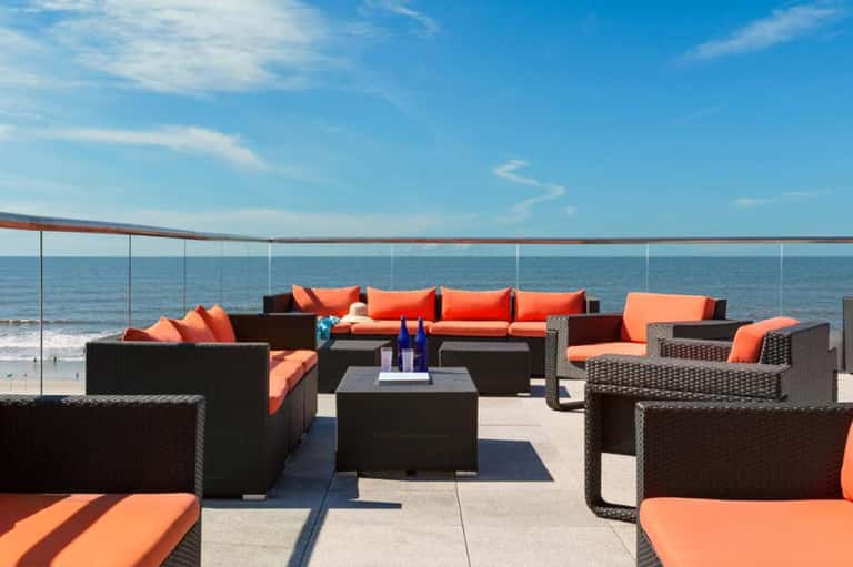 Beachfront lounge area with black wicker furniture and orange cushions facing the ocean