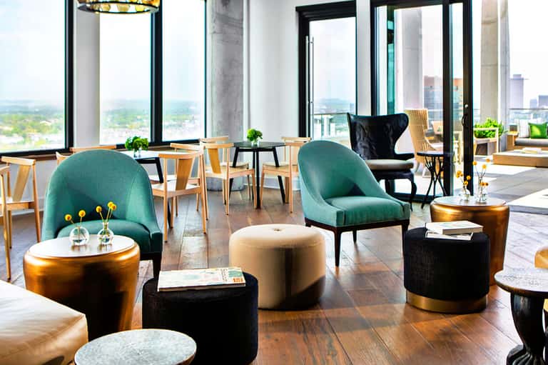Upscale lounge with teal chairs, gold side tables, wooden flooring, and panoramic city views