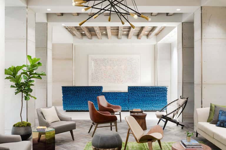 Modern hotel lobby with blue woven seating, wooden ceiling beams, and contemporary furniture arrangement