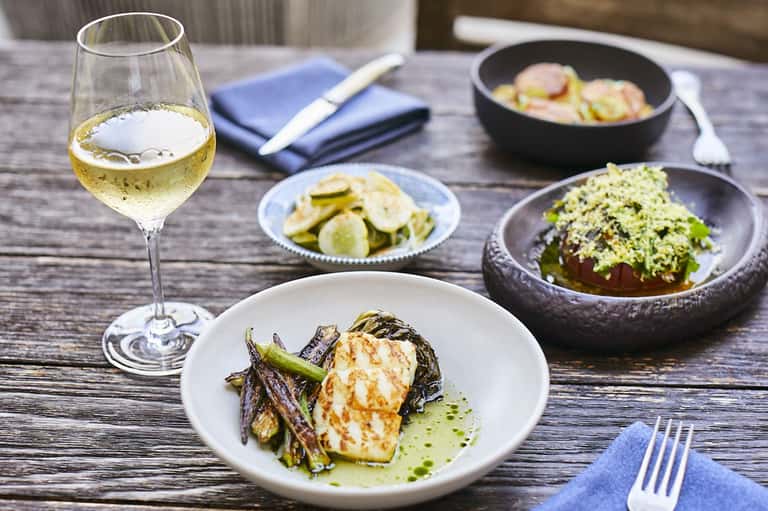 White wine glass with plated halibut and green sauce at outdoor dining table