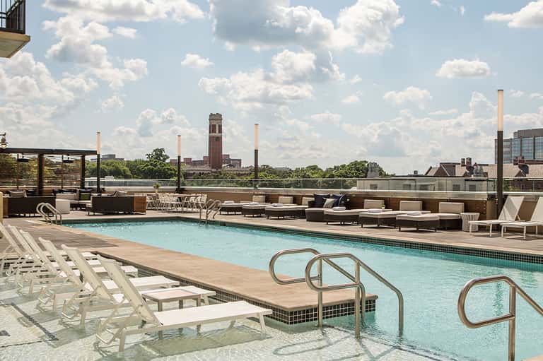 Rooftop pool deck with lounge chairs, umbrellas, and city skyline views including historic tower