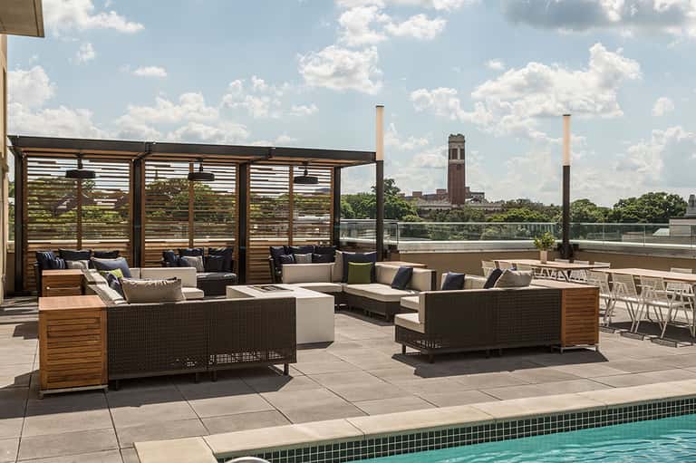 Rooftop terrace with woven lounge seating, wooden pergolas, and city skyline view in background