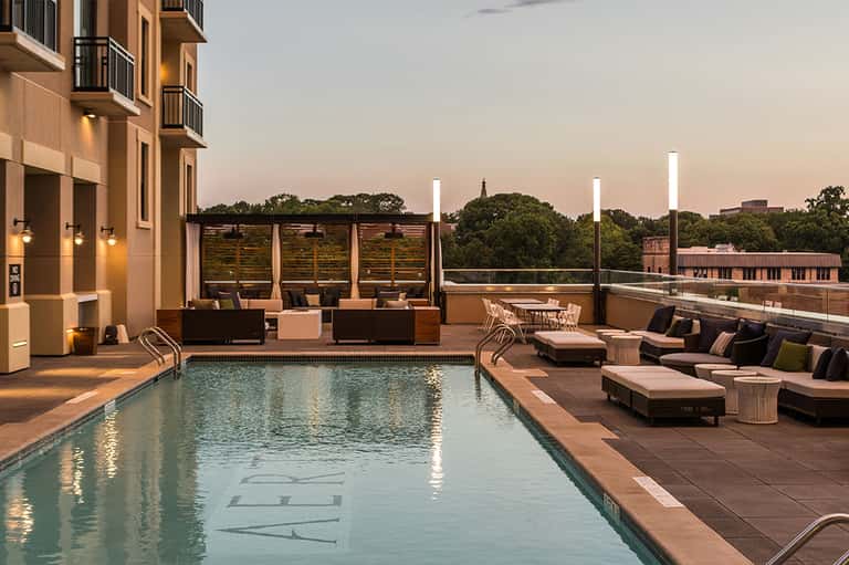 Rooftop pool deck at dusk with lounge chairs, ambient lighting, and city skyline views