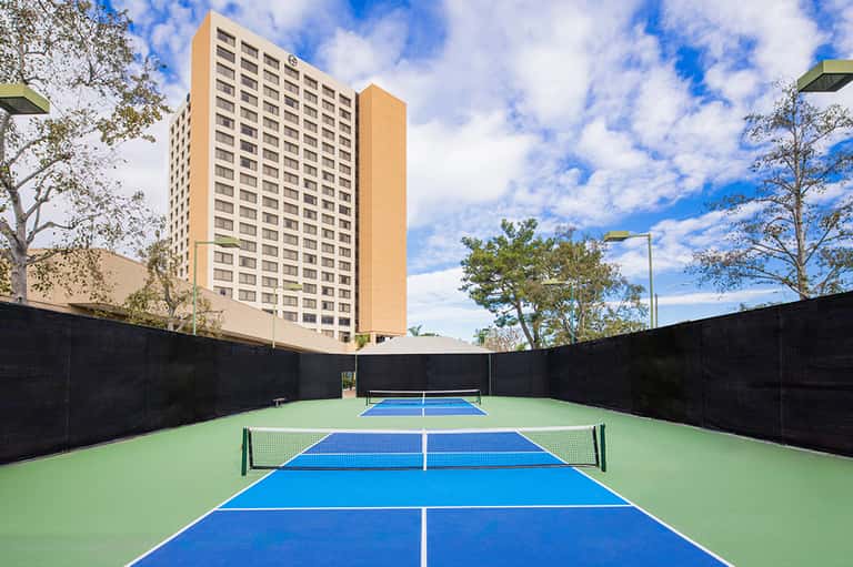 Tennis courts with blue and green surfaces surrounded by black netting near tall residential building