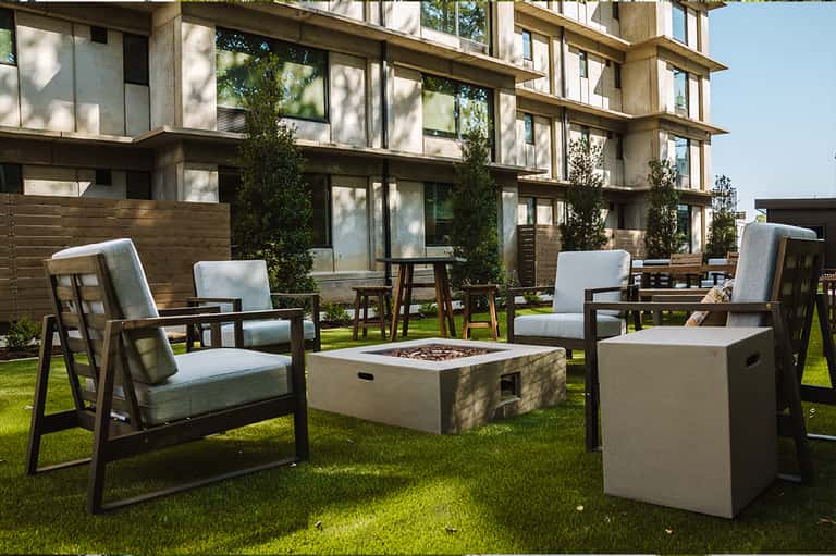 Modern outdoor patio with lounge chairs, fire pit, and contemporary apartment building