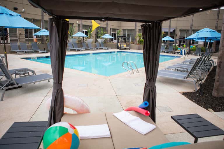 Shaded poolside area with lounge chairs, umbrellas, and colorful pool floats