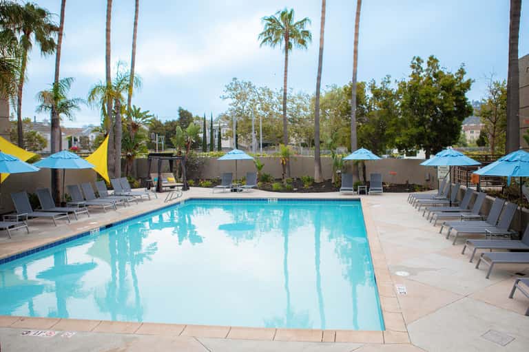 Resort swimming pool surrounded by palm trees, blue umbrellas, and lounge chairs