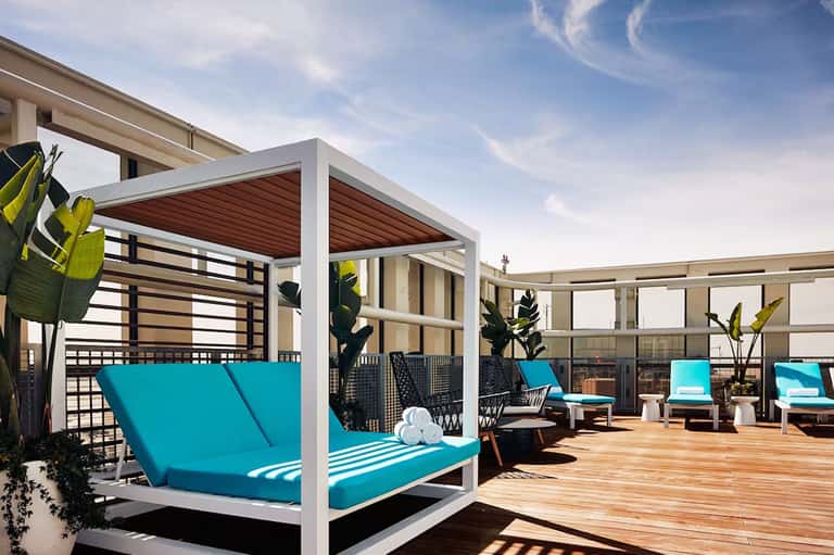 Modern rooftop deck with white pergola, turquoise loungers, wooden decking, and city views