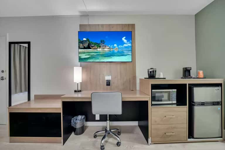 Hotel room workspace with desk, chair, and beach scene displayed on wall-mounted TV