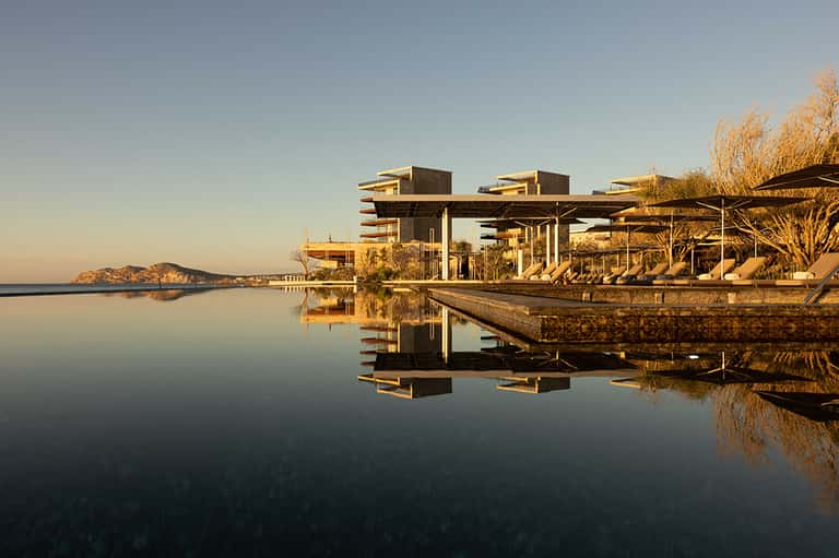 Modern spa building reflected in still water at golden hour with island landscape in background