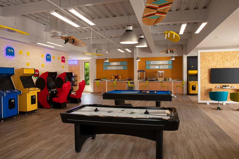 Colorful indoor game room with arcade games, pool tables, air hockey, and Pac-Man themed decor