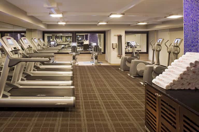 Modern fitness center with treadmills, ellipticals, and rolled towels on shelf