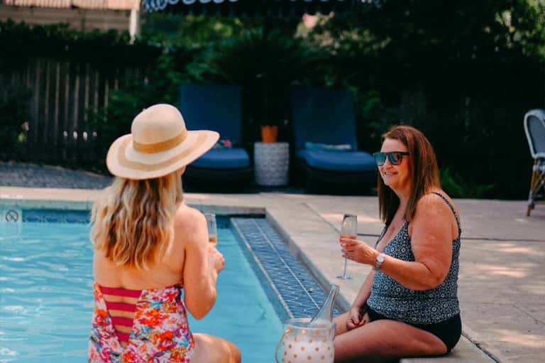 Two women relaxing by pool, one wearing hat and floral swimsuit, other in sunglasses