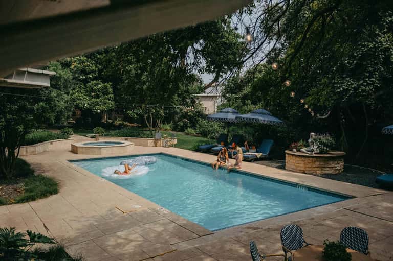 Backyard resort pool with lounge chairs, hot tub, and lush green trees surrounding the deck area