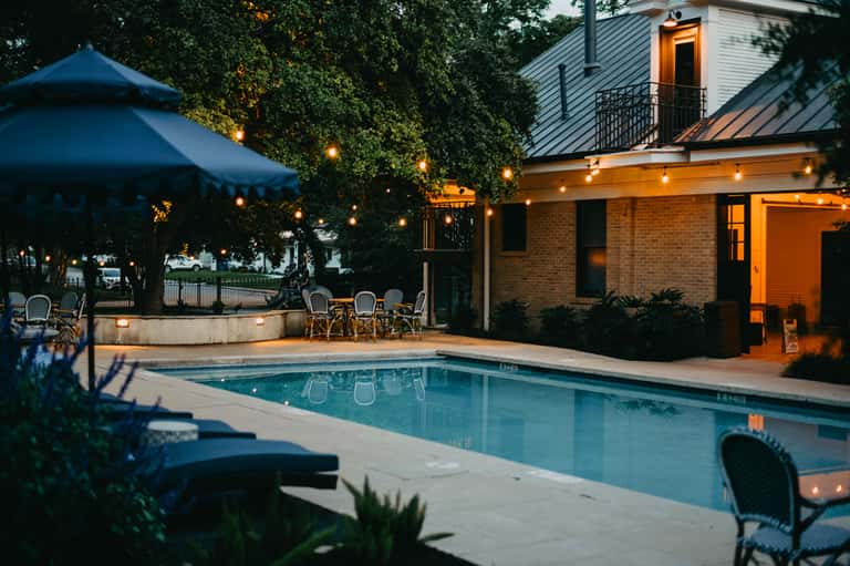 Luxury resort pool at dusk with string lights, brick building, and covered seating area