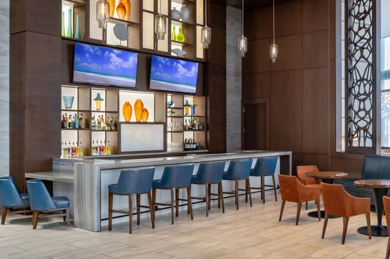 Modern hotel bar with blue seating, wooden countertop, and shelving displaying spirits