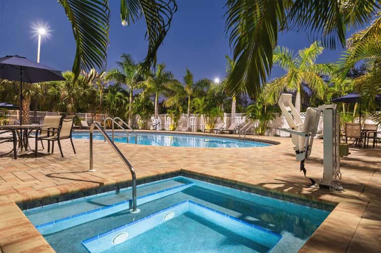 Resort pool area at dusk with palm trees, loungers, and hot tub