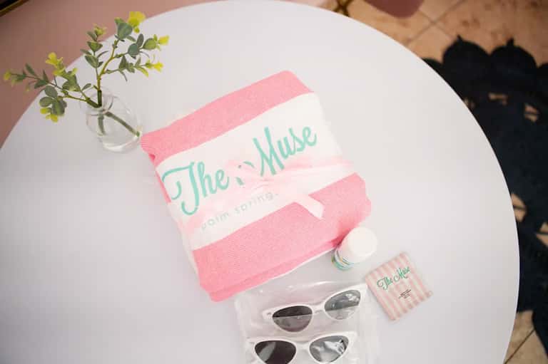 White table with pink towel branded 'The Muse', sunglasses, and small toiletries on display