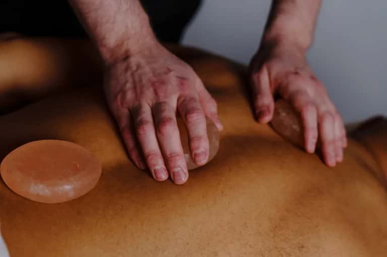 Hands performing massage therapy on person's back with massage stone