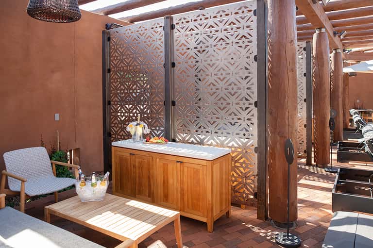 Terracotta patio with wooden bar, decorative lattice screens, wooden lounge chair, and woven pendant light fixture