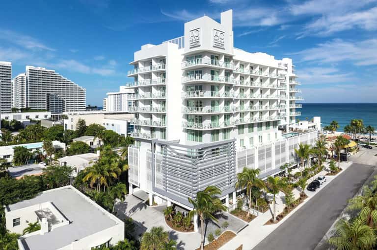 Modern beachfront hotel building with white architecture and balconies overlooking ocean and palm trees