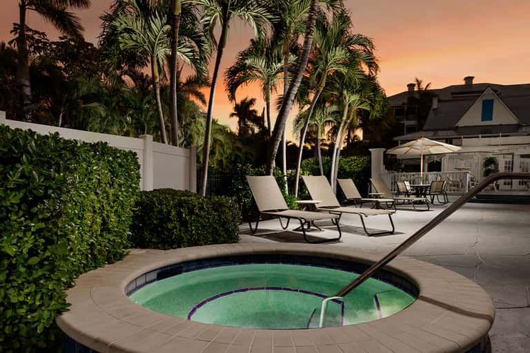 Spa hot tub at dusk surrounded by lounge chairs, palm trees, and modern residential architecture at sunset