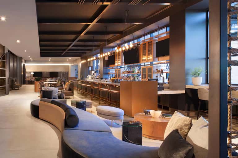 Modern hotel lounge with curved seating, wooden bar, hanging pendant lights, and sophisticated ambiance
