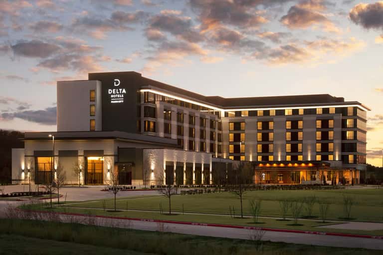 Modern Delta Hotels building exterior at dusk with illuminated windows and manicured landscape