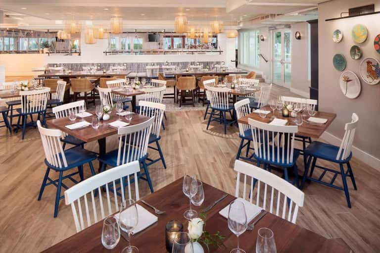 Upscale restaurant dining room with wooden tables, white and blue chairs, and pendant lighting
