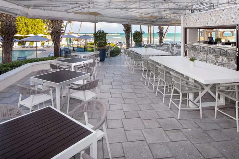 Modern outdoor dining pavilion with white tables and chairs overlooking pool and ocean