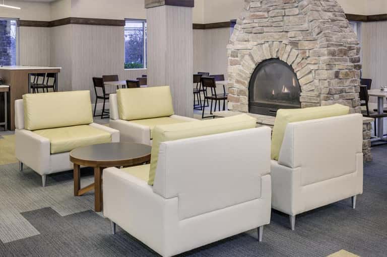 Modern lounge area with cream upholstered chairs, wooden side table, and stone fireplace with gas insert