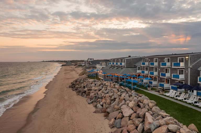 Beachfront resort at sunset with rocky seawall, sand beach, and multi-story blue-accented buildings