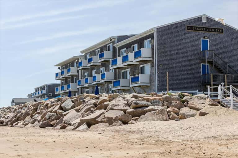 Pleasant View Inn beachfront building with blue balconies on sandy shore with boulder breakwater