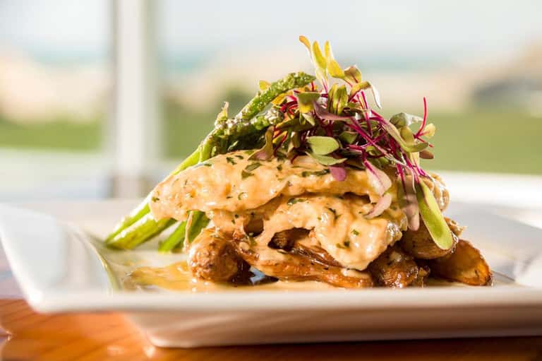 Plated seafood dish with greens and microgreens on white plate overlooking ocean