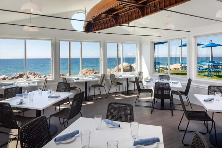 Modern beachfront dining room with floor-to-ceiling windows overlooking ocean and rocky coastline