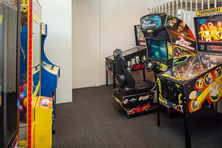 Game room with vintage arcade machines including Fast & Furious and pinball games on dark flooring