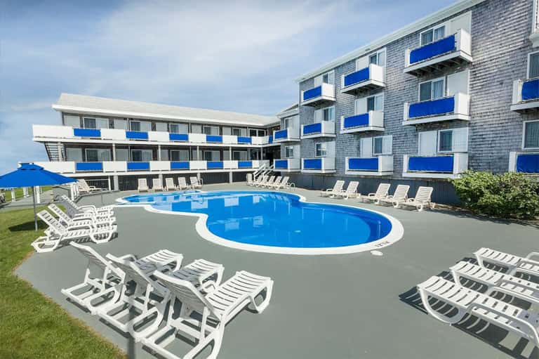 Large blue swimming pool with white loungers in front of beachfront hotel building