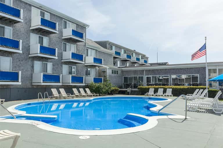 Outdoor pool with blue water and white lounge chairs, multi-story hotel building with blue balconies and American flag