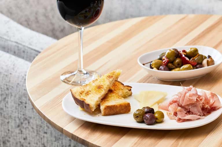 Wine glass, charcuterie board with cured meats, cheese, and olives on wooden table